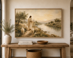 A large framed landscape painting hangs on a beige wall above a rustic wooden console table. The painting depicts a shepherd with sheep near a river in a warm, golden-toned scene.