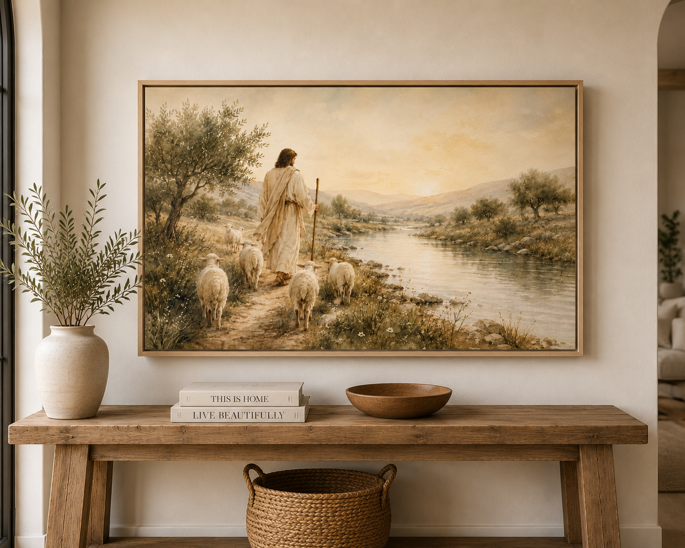 A large framed landscape painting hangs on a beige wall above a rustic wooden console table. The painting depicts a shepherd with sheep near a river in a warm, golden-toned scene.