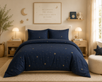 A navy blue bedding set with a starry night sky pattern is styled on a bed in a warm, cozy bedroom. The set includes a duvet cover and two matching pillowcases, decorated with small gold stars and larger glowing starburst motifs.
