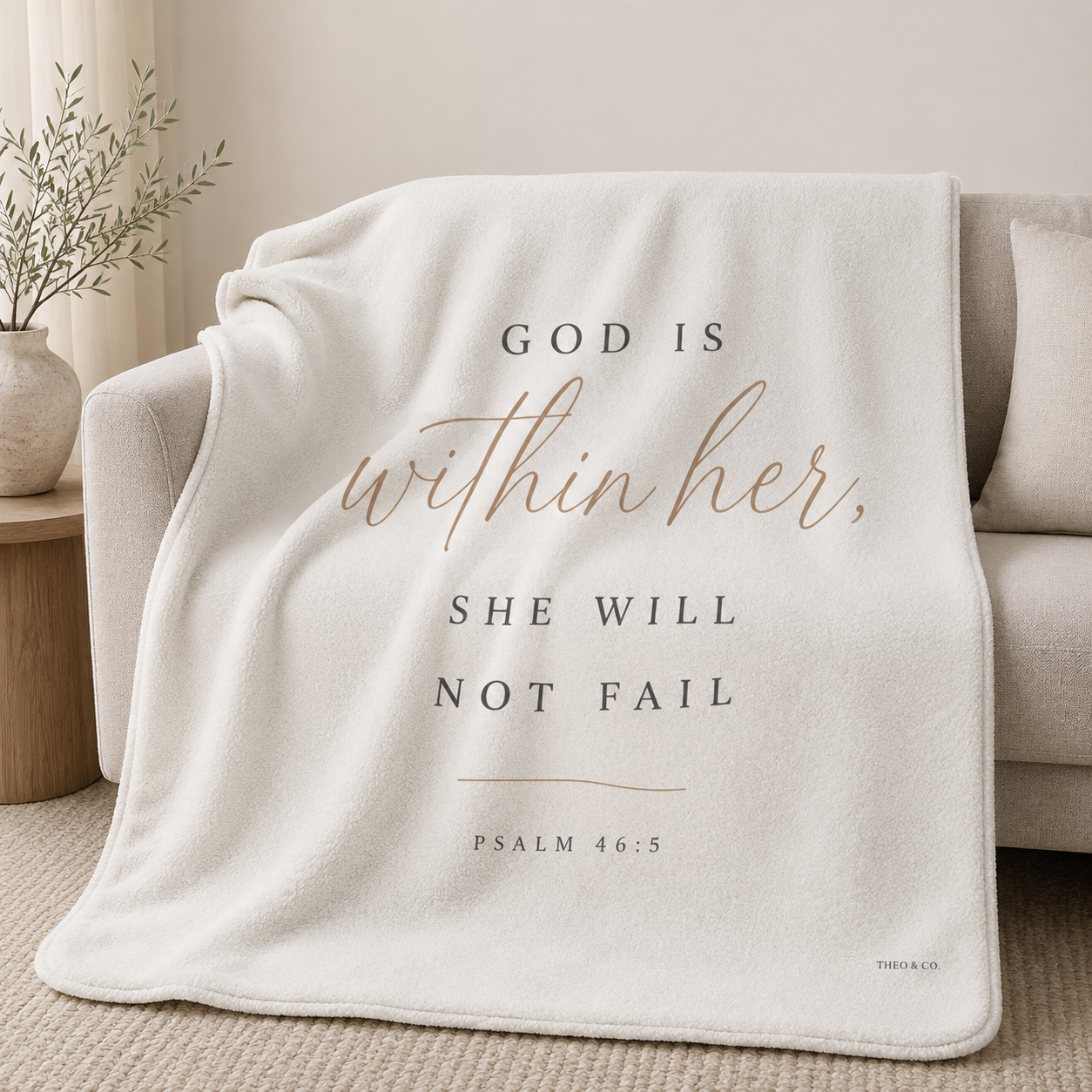 An off-white fleece throw blanket draped over a light beige sofa in a neutral living room setting. The blanket features the printed text 'GOD IS within her, SHE WILL NOT FAIL' and 'PSALM 46:5' in dark gray lettering, with 'within her' in a warm rose-gold script.