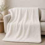 A soft cream-colored fleece throw blanket draped over a light beige sofa in a minimalist living room setting.