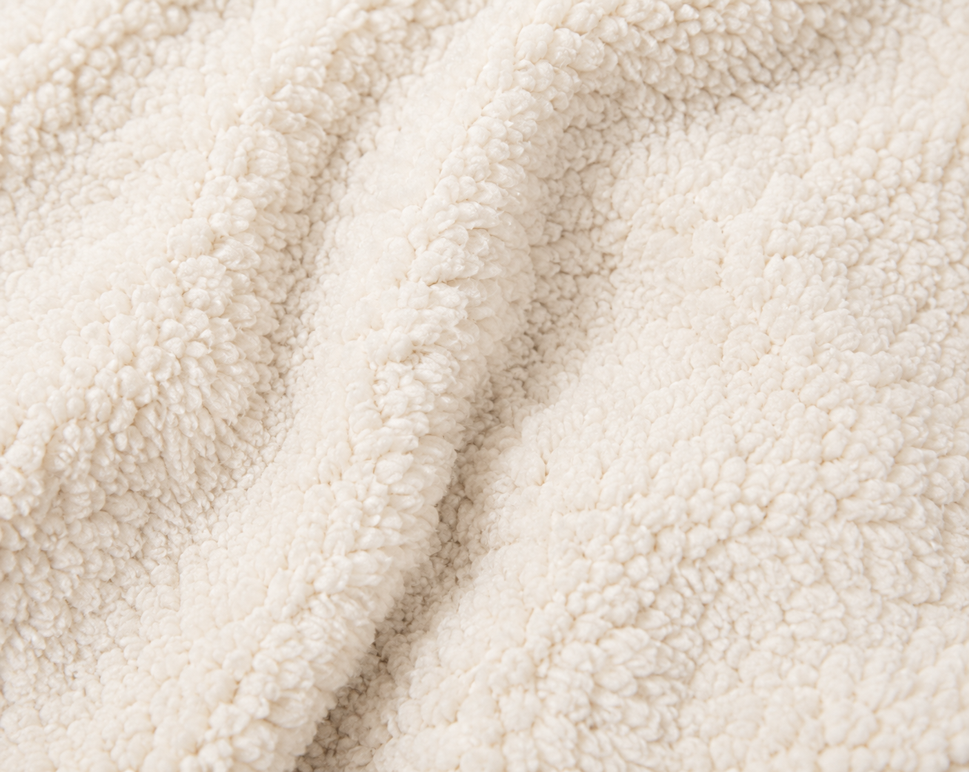 Close-up of a soft, plush sherpa fabric in a warm off-white or cream color, showing the textured pile and gentle folds.