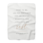 A white rectangular blanket with rounded corners featuring a printed Bible verse from Matthew 11:28. The text reads 'COME TO ME, ALL YOU WHO LABOR AND ARE HEAVILY BURDENED, AND I WILL GIVE YOU rest.