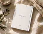 A white hardcover notebook or journal with the name 'Alexander Smith' and 'THIO & CO.' printed on the cover, styled on a beige linen surface with a ceramic bowl and green leaves nearby.