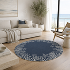 A round navy blue area rug with a white starfish and coral pattern, styled in a bright, modern living room with a beige sofa and a large window overlooking the ocean.