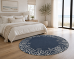 A round navy blue area rug with a white starfish and coral pattern, styled in a bright, modern bedroom next to a bed with neutral bedding.