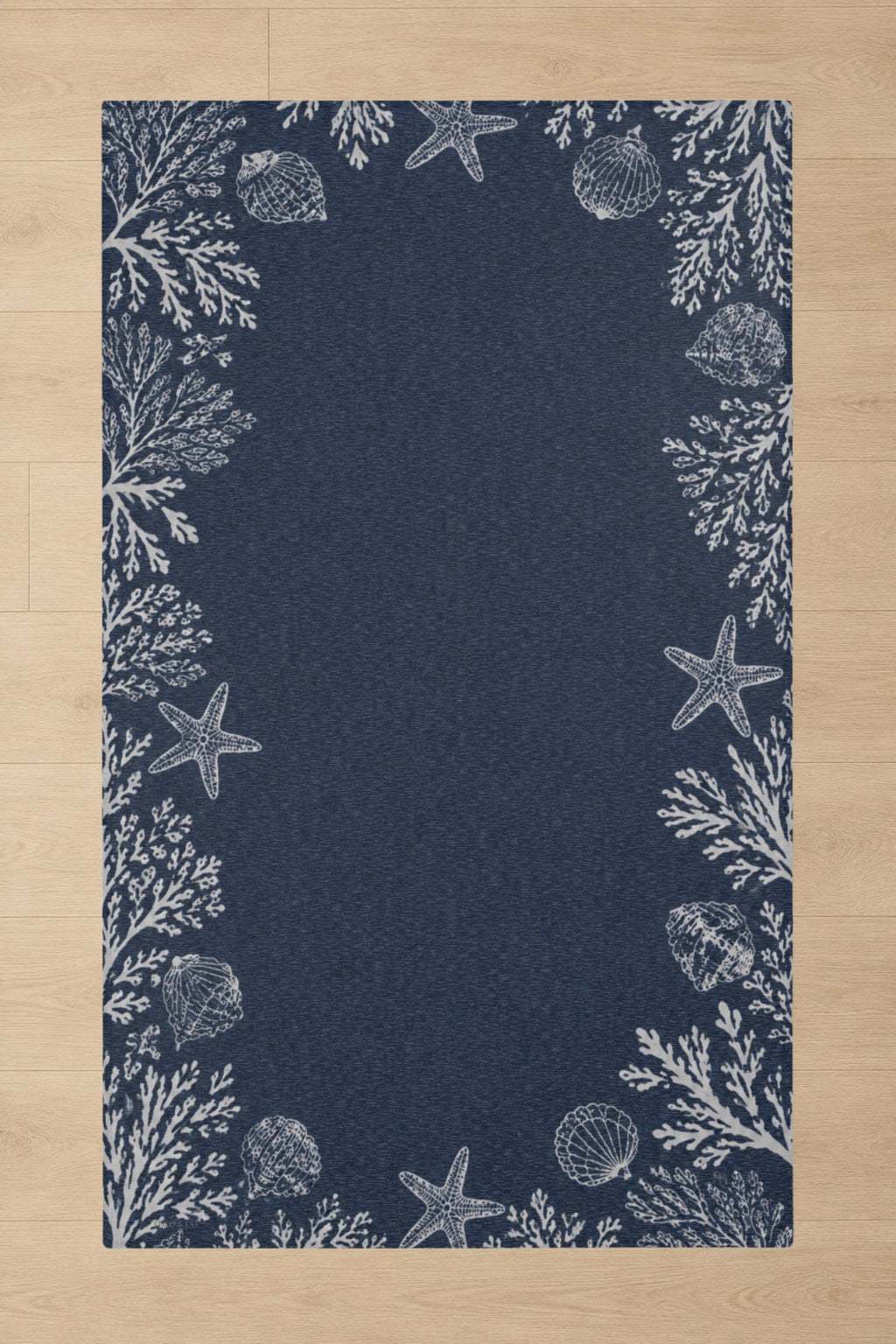 A rectangular navy blue rug with a white nautical border featuring starfish, seashells, and coral, shown flat on a light wood floor.