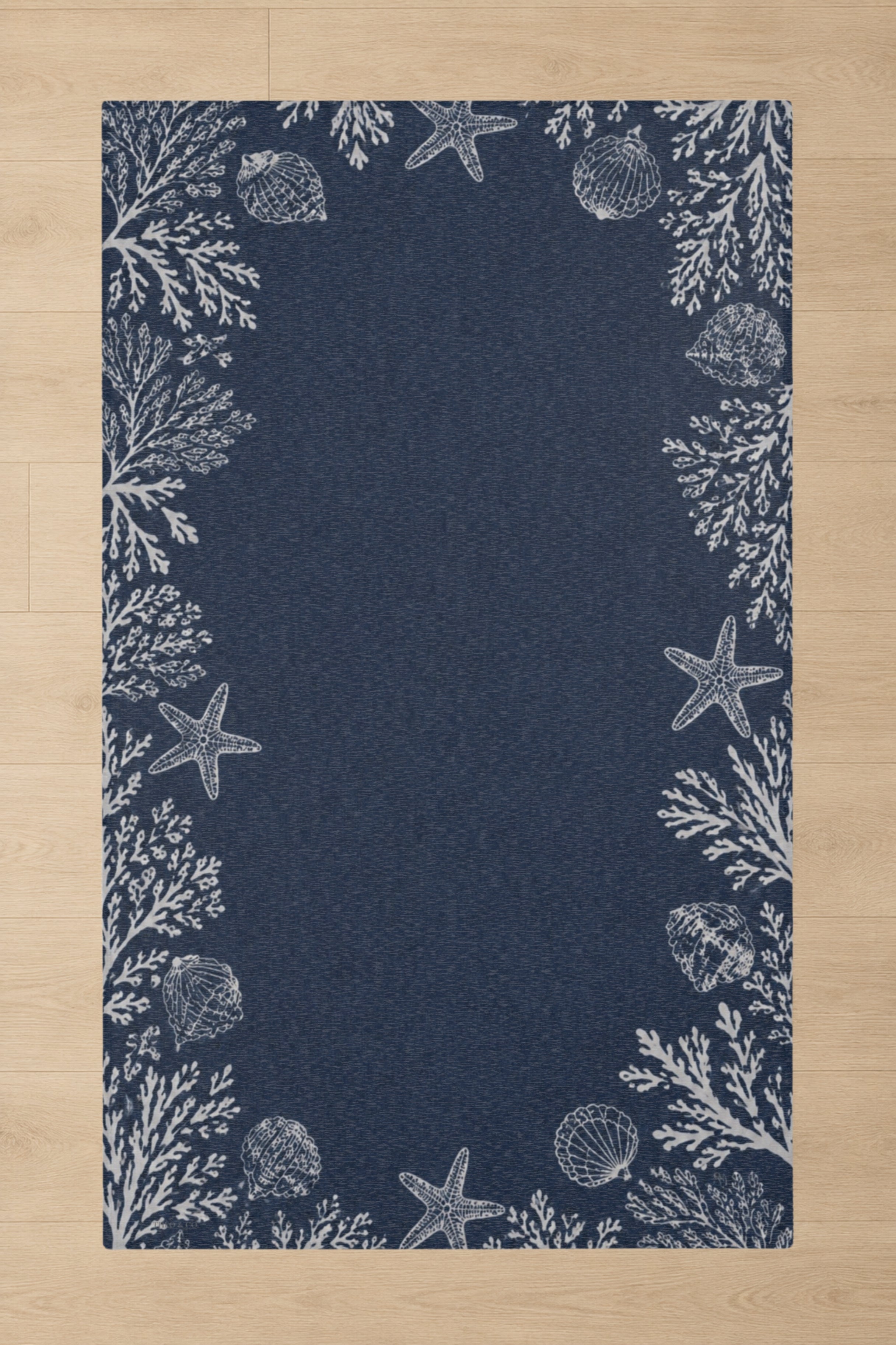 A rectangular navy blue rug with a white nautical border featuring starfish, seashells, and coral, shown flat on a light wood floor.