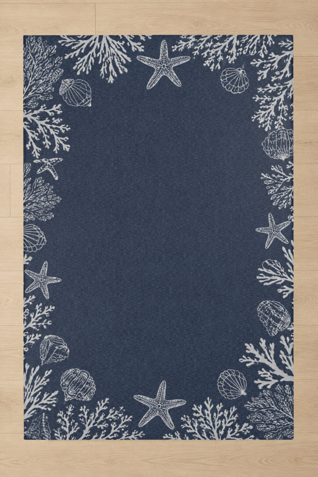 A rectangular navy blue rug with a white seashore print featuring starfish, shells, and coral, laid flat on a light wood floor.