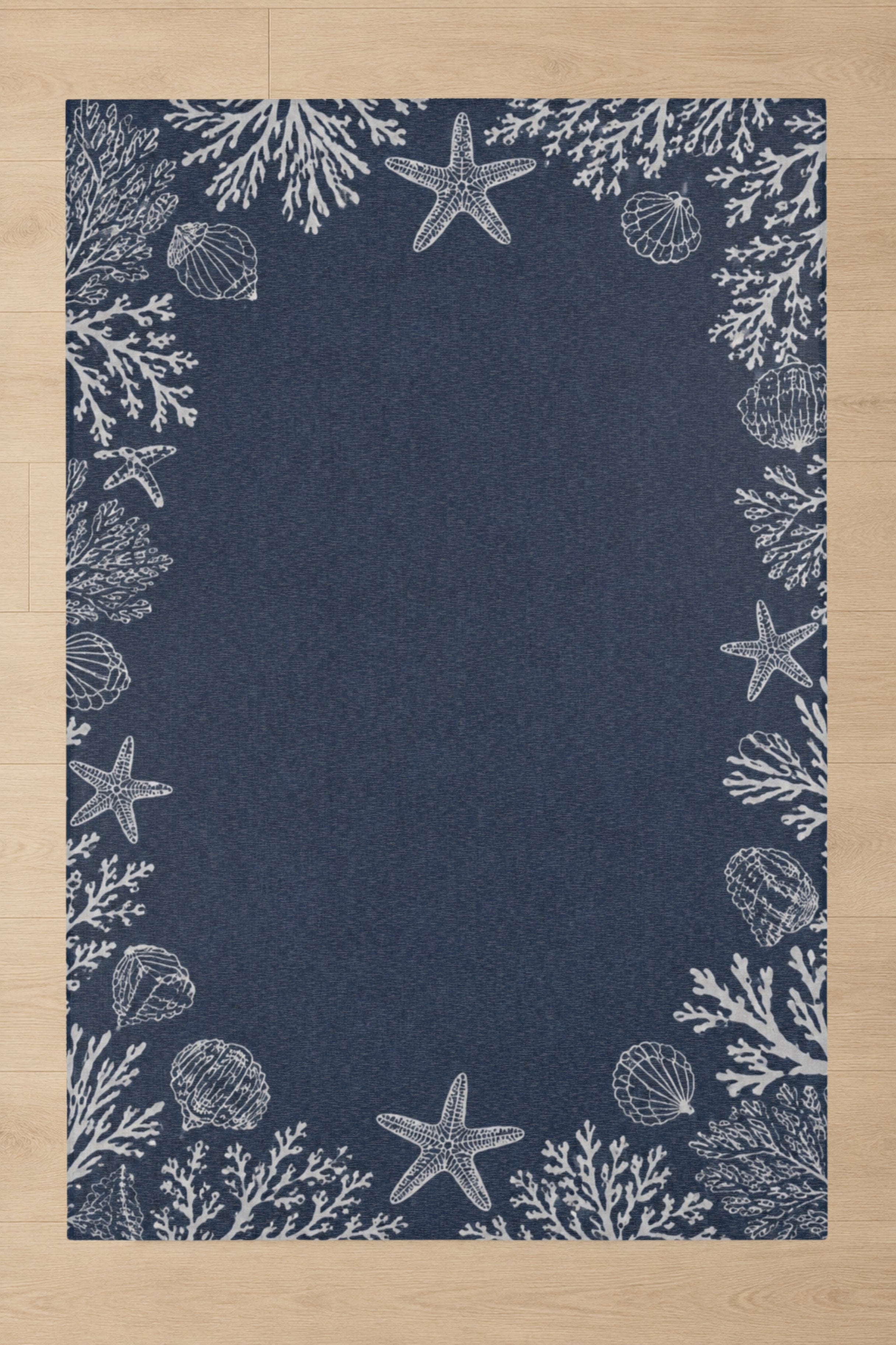 A rectangular navy blue rug with a white seashore print featuring starfish, shells, and coral, laid flat on a light wood floor.