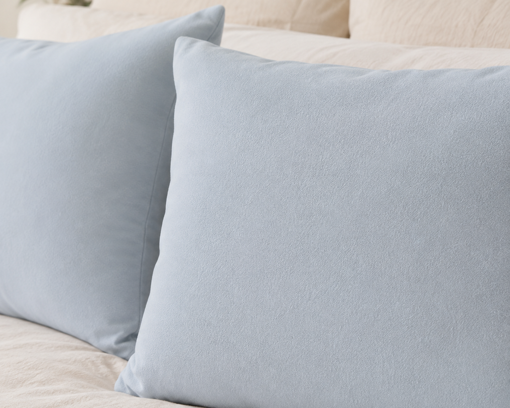 Two light blue pillows resting on a cream-colored bed or sofa.
