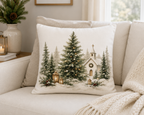 A square decorative throw pillow with a Christmas village scene printed on it, resting on a light beige sofa in a cozy living room setting.
