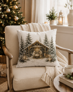 A square decorative throw pillow featuring a Christmas nativity scene print, styled on a beige armchair in a cozy living room with a Christmas tree, blanket, and window in the background.