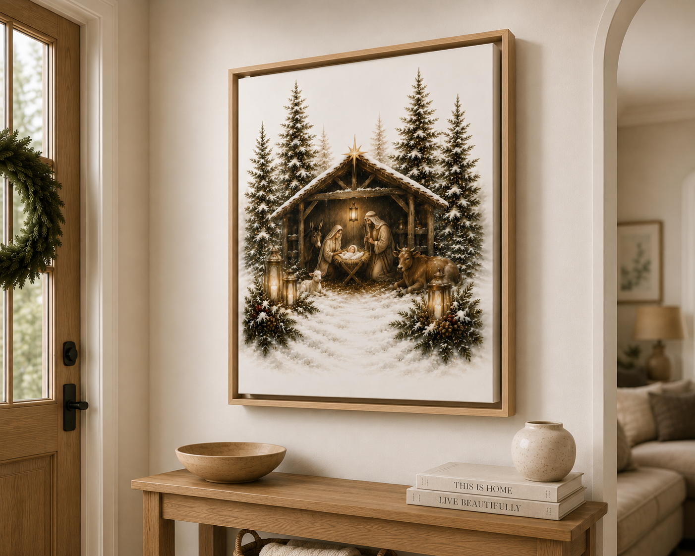 A framed Christmas nativity scene print hangs on a beige wall above a wooden console table in a styled home interior. The artwork shows a snowy stable with pine trees, warm lantern light, and figures in a rustic scene.