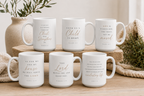 Six white ceramic mugs with gold and black Bible verse quotes, arranged on wooden blocks and a light wood surface with neutral home decor props.