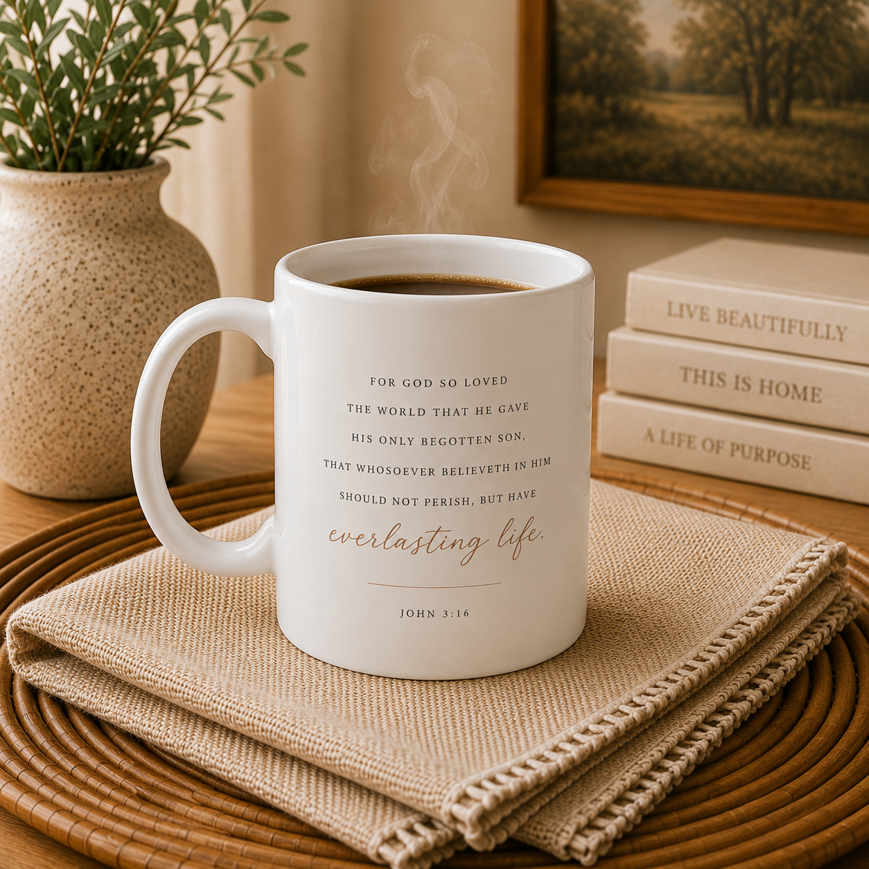 A white ceramic coffee mug with a Bible verse printed on it, sitting on a woven placemat with a burlap napkin. The mug is styled in a cozy home setting with a potted plant, books, and a framed picture in the background.