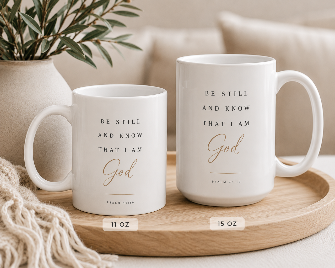 Two white ceramic mugs with black and gold Bible verse text, displayed on a wooden tray in a cozy home setting. One mug is labeled 11 oz and the other 15 oz.