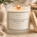 A lit vanilla scented candle in a frosted glass jar with a wooden wick, featuring a white label with black text that reads 'THEO & CO. AS FOR ME AND MY HOUSE, WE WILL SERVE THE LORD.