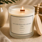 A lit glass jar candle with a wooden wick and a cream label reading 'THEO & CO. THE LORD BLESS YOU, AND KEEP YOU.
