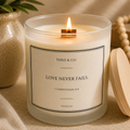 A lit vanilla scented candle in a frosted glass jar with a cream label reading 'THEO & CO. LOVE NEVER FAILS.