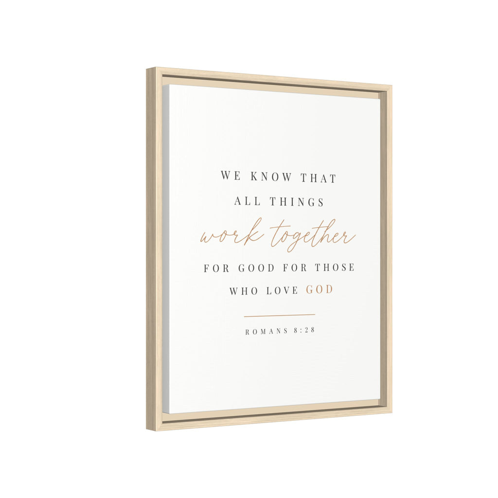 Framed wall art print with the Bible verse Romans 8:28, featuring elegant black and rose gold typography on a clean white background, housed in a light natural wood frame.