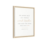 Framed wall art print with the Bible verse Romans 8:28, featuring elegant black and rose gold typography on a clean white background, housed in a light natural wood frame.