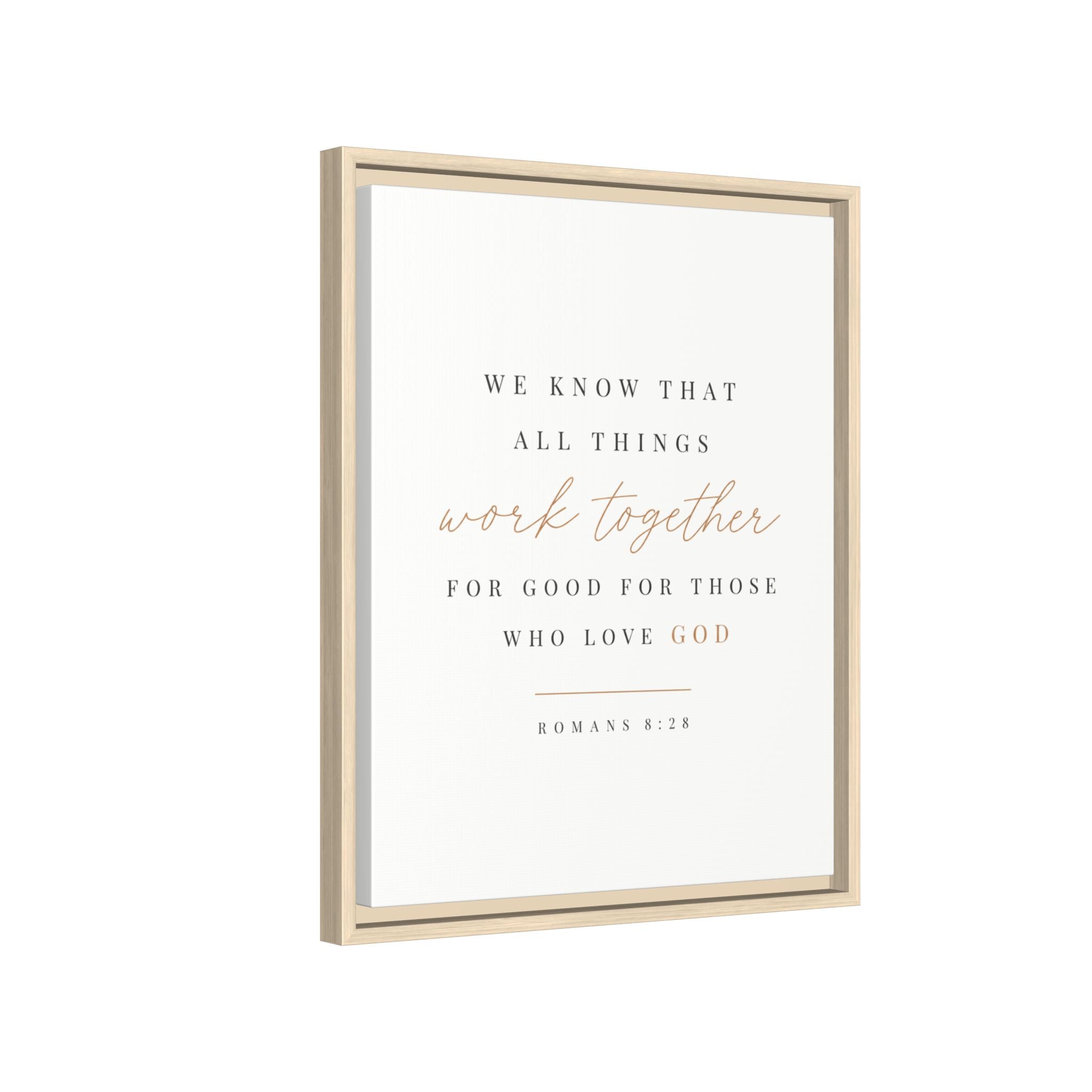 Framed wall art print with the Bible verse Romans 8:28, featuring elegant black and rose gold typography on a clean white background, housed in a light natural wood frame.