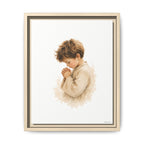 A framed art print featuring a watercolor-style illustration of a young child in a cream robe, shown against a white background with a light wood frame.