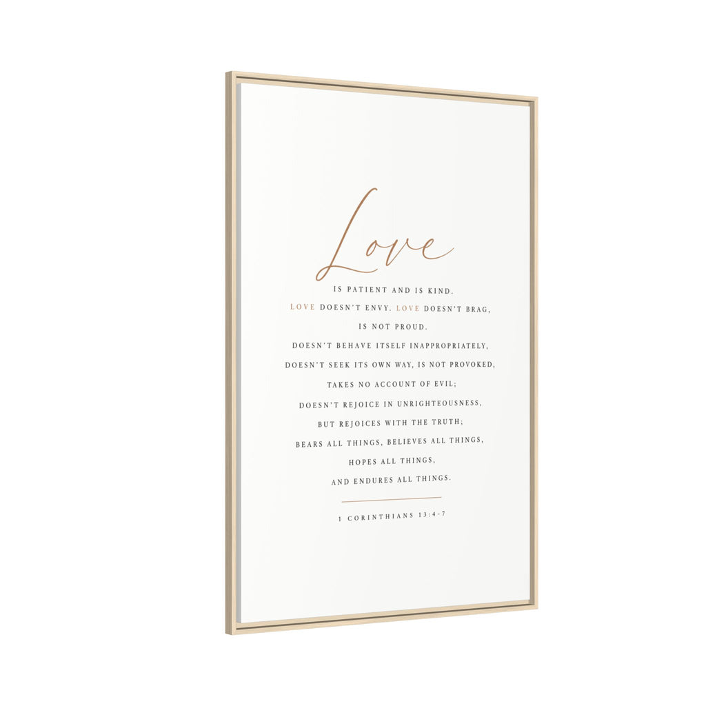 A vertical framed art print featuring the word 'Love' in elegant rose-gold script above a printed Bible verse in dark gray text on an off-white background, enclosed in a thin light wood frame.