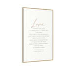 A vertical framed art print featuring the word 'Love' in elegant rose-gold script above a printed Bible verse in dark gray text on an off-white background, enclosed in a thin light wood frame.