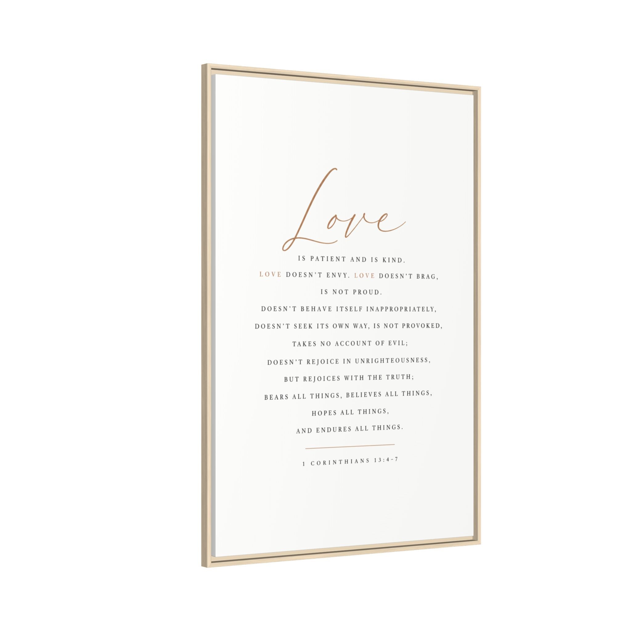 A vertical framed art print featuring the word 'Love' in elegant rose-gold script above a printed Bible verse in dark gray text on an off-white background, enclosed in a thin light wood frame.