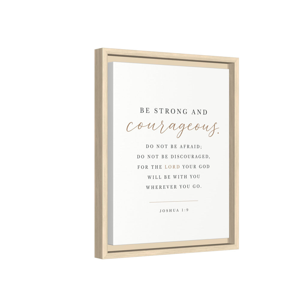 A framed wall art print featuring the Bible verse Joshua 1:9. The print has a white background with black serif text and the word 'courageous' in a metallic rose-gold script.
