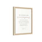 A framed wall art print featuring the Bible verse Joshua 1:9. The print has a white background with black serif text and the word 'courageous' in a metallic rose-gold script.