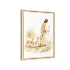 Framed wall art featuring a soft watercolor-style illustration of Jesus walking with two sheep, shown in a light wood frame against a plain white background.
