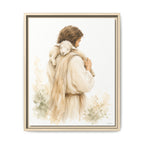 A framed watercolor-style art print showing a man in soft beige robes carrying a white sheep on his shoulders, set against a clean white background.