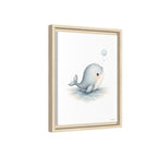 A framed art print featuring a cute, stylized illustration of a light blue-gray beluga whale blowing a bubble, set in a light natural wood frame against a white background.