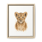 A framed watercolor-style art print featuring a lion cub centered on a white background, with a light wood frame and dark inner trim, shown against a plain white wall.