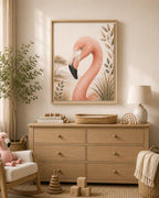 A framed art print of a pink flamingo hanging on a beige wall above a light wood dresser in a styled nursery or children's room. The room includes a matching pink plush toy, a white rocking chair, a lamp, and wooden toys.