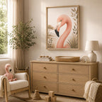 A framed art print of a pink flamingo with botanical leaves, displayed on a light wood dresser in a styled nursery room with a rocking chair, lamp, and plant.